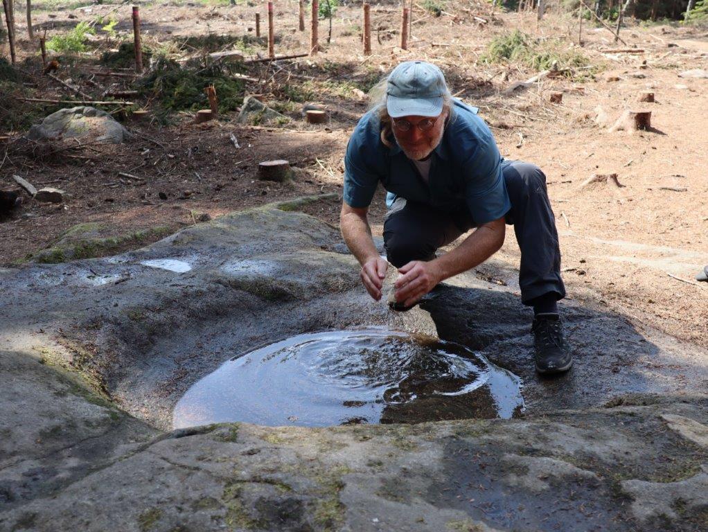 Ein mann wäscht sich in einer mit Wasser gefüllten Gesteinsmulde