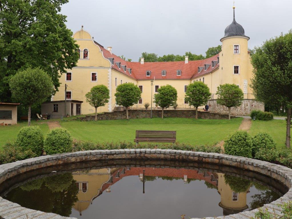 Kreisrundes Wasserbecken in einem Garten, dahinter ein Schlossgebäude